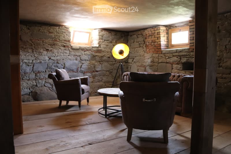 Cozy living room with exposed stone walls, wooden floor, sofa, armchair, coffee table, and floor lamp.