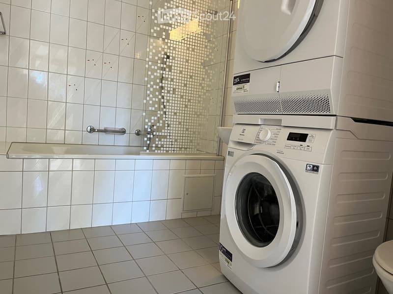 Modern bathroom with white tiled walls, a shower area, a washing machine, and a bathtub.