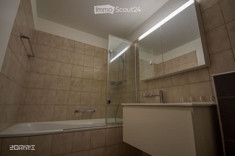 Modern bathroom with beige tiled walls, a bathtub, a sink with a mirror, and a glass-enclosed shower stall.