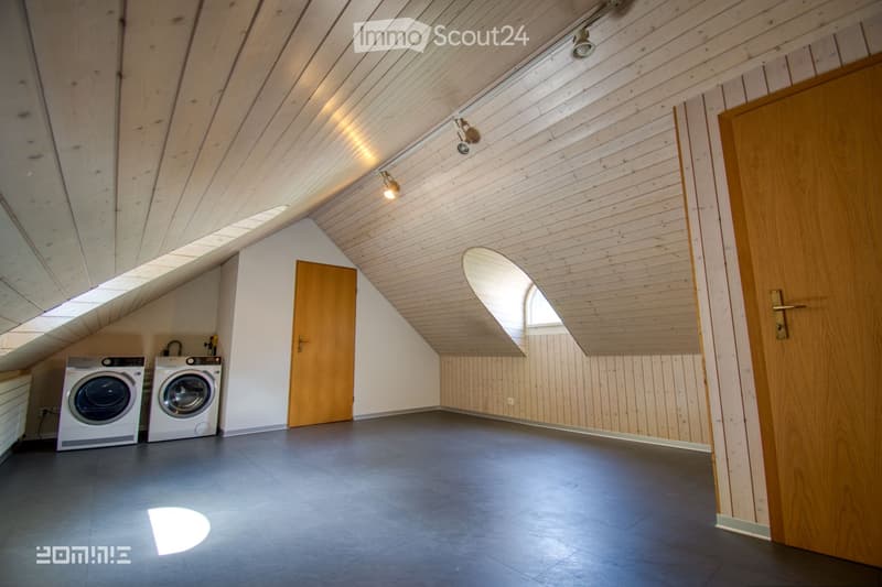 Attic room with wooden walls and ceiling, two washing machines, and a door leading to another area.
