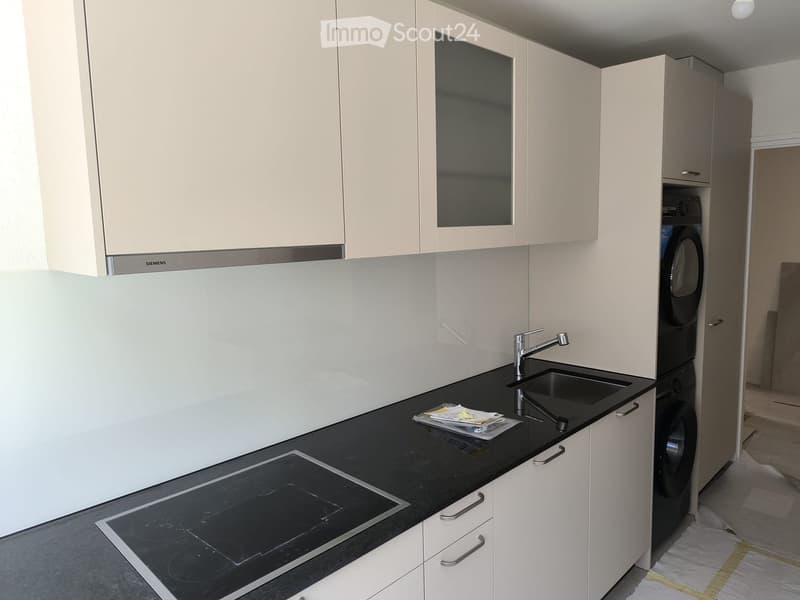 Modern kitchen with white cabinets, black countertop, induction cooktop, sink, and a washing machine in the corner.