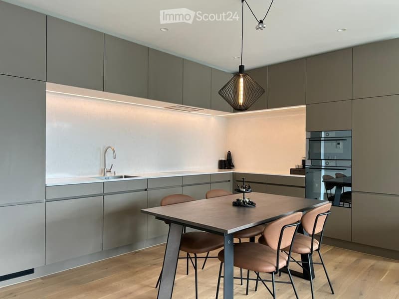 modern kitchen with wooden floor, gray cabinets, white countertops, stainless steel sink, faucet, dining table with chairs, hanging lamp, built-in oven