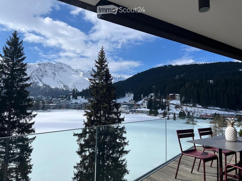 glass railing, wooden floor, table with chairs, glass table top, view of snowy mountains and lake