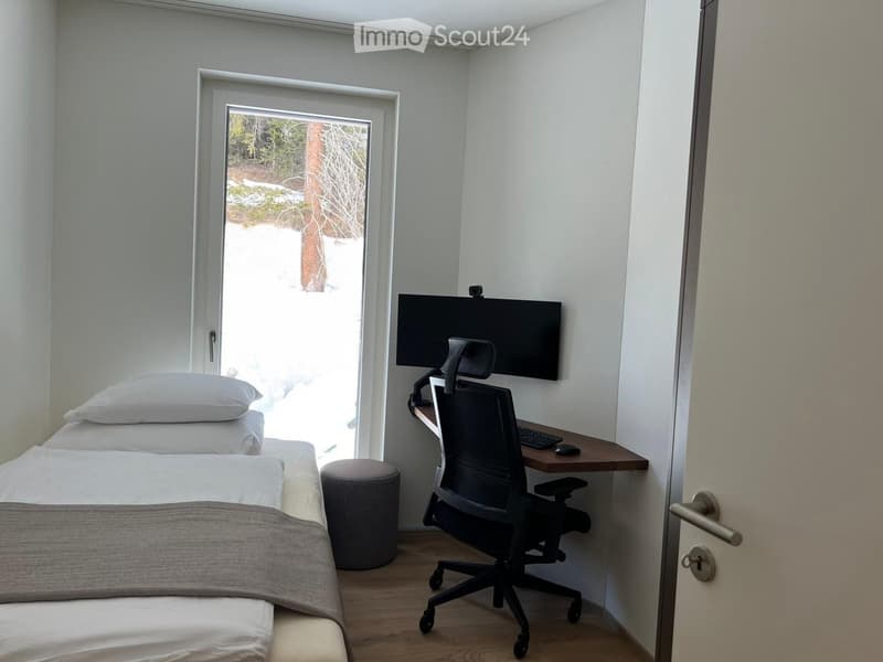 small bedroom with a bed, desk, chair, monitor, keyboard, mouse, ottoman, and a window with a view of the outside