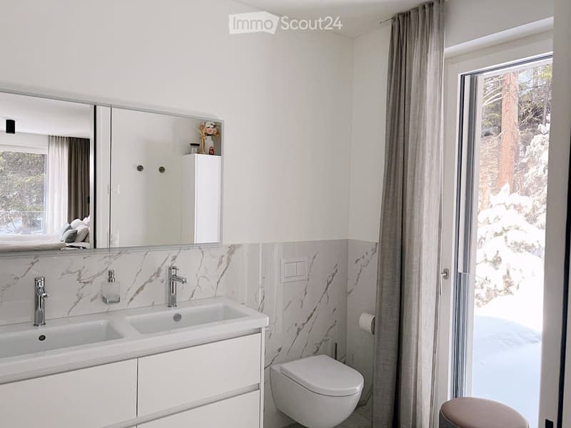 modern bathroom with white marble tiles, double sink, mirror, toilet, window with snowy view