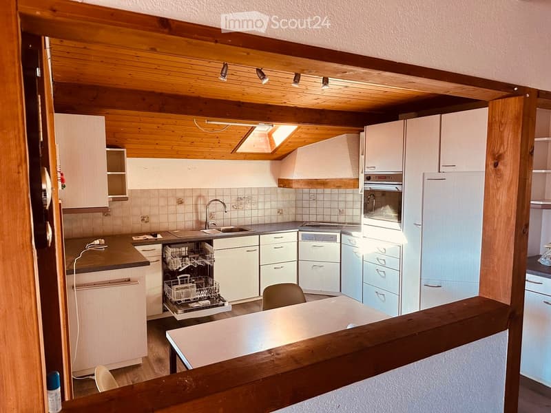 Modern kitchen with white cabinets, stainless steel appliances, wooden ceiling, and a small dining area.