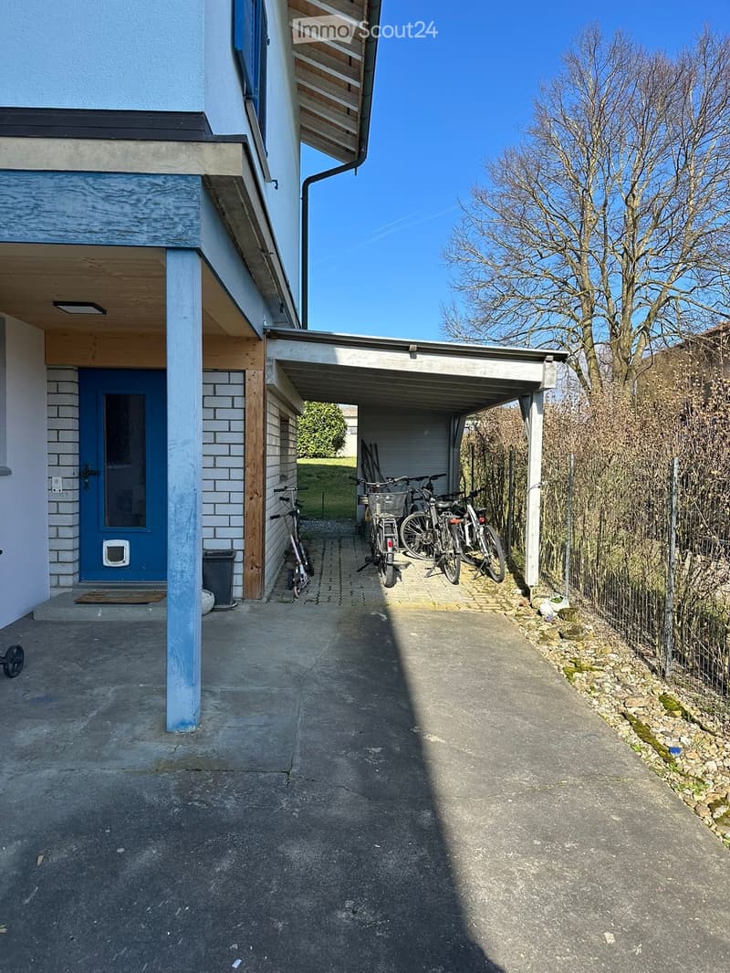 A modern two-story house with a covered driveway, bicycles parked inside, and a blue front door.