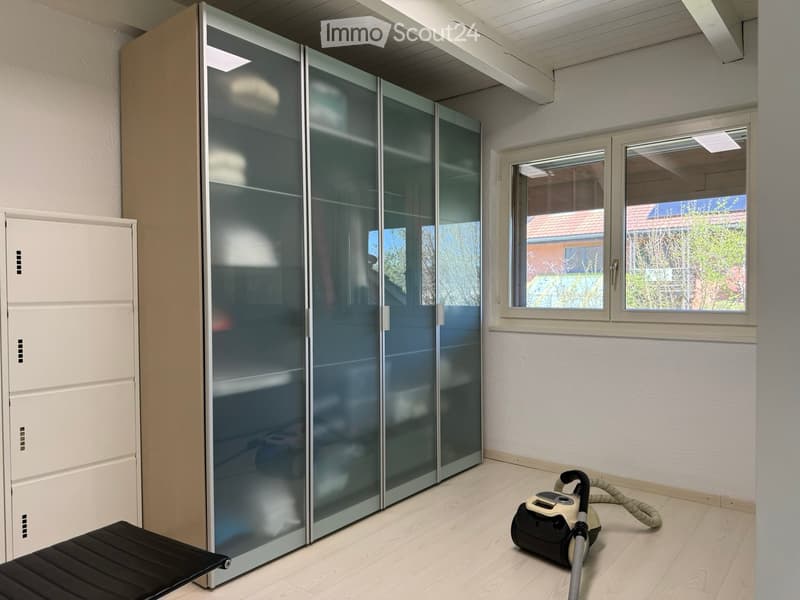 The image shows a bedroom with a large built-in wardrobe with frosted glass doors, hardwood flooring, and a window overlooking the outdoors. The room appears to be clean and well-lit.