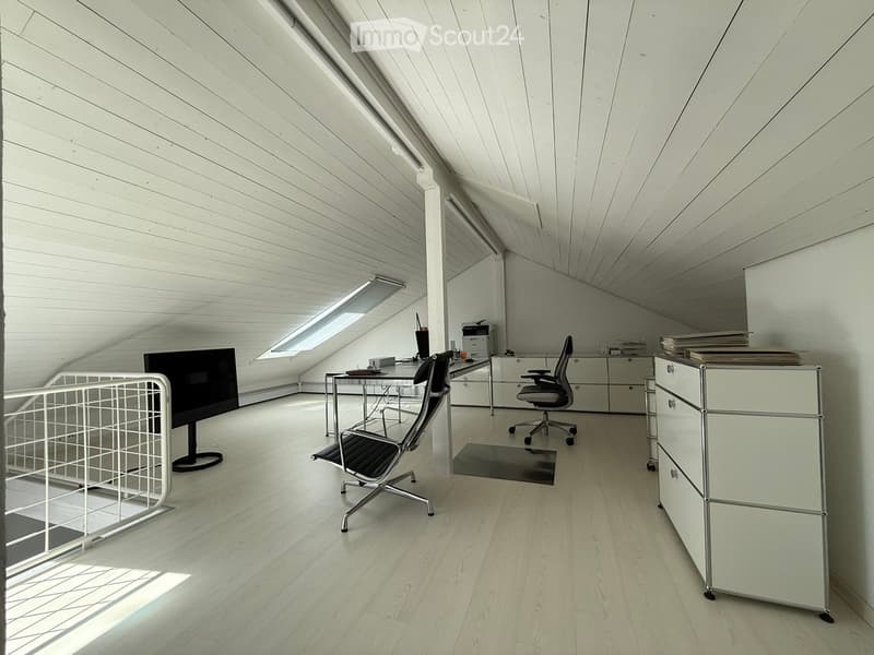 Attic office space with slanted ceiling, white walls, hardwood flooring, desk with computer setup, office chair, storage cabinets, and a wire mesh storage unit.