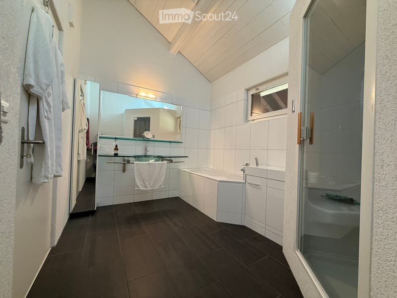 Spacious bathroom with white tiled walls, dark tile flooring, a bathtub, vanity with mirror, and a private washing machine