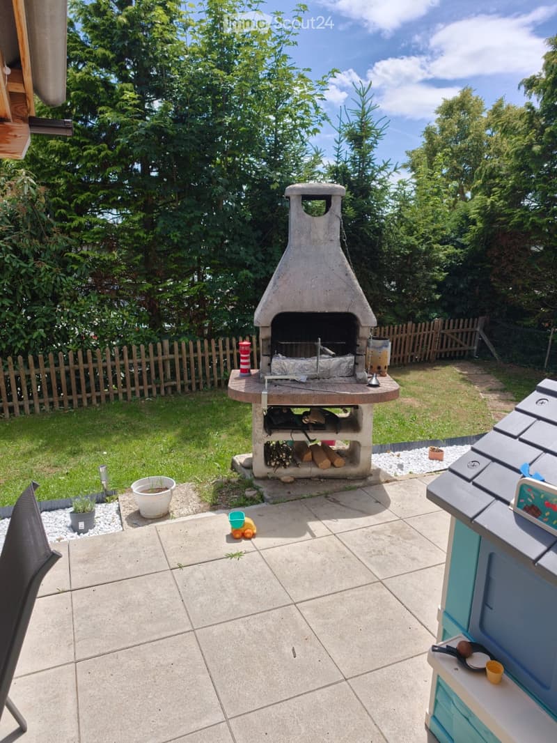 Garden area with a stone barbecue, a small table, a chair, a toy, and potted plants.