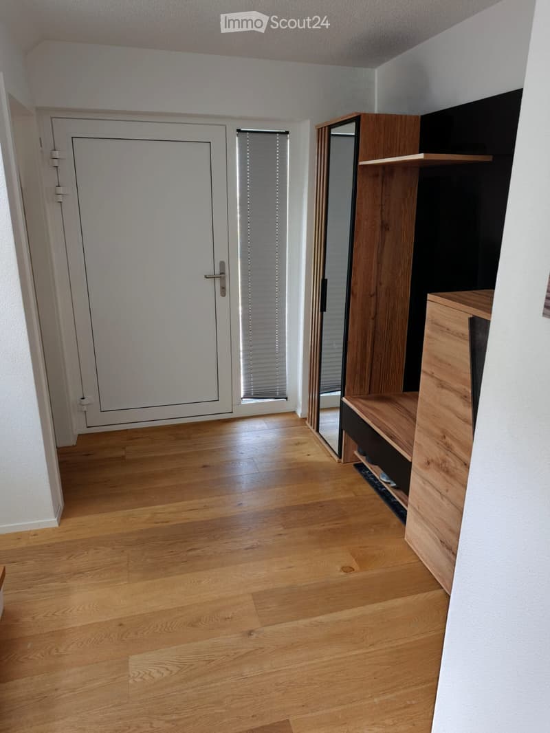 Empty hallway with wooden flooring, white walls, a white door, and a wooden shoe rack with a mirror.