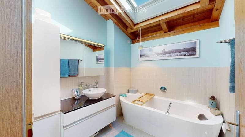Bright bathroom with a wooden slanted ceiling, a large window, a white sink with a modern faucet, a bathtub, a mirror, and a towel rack with blue towels.