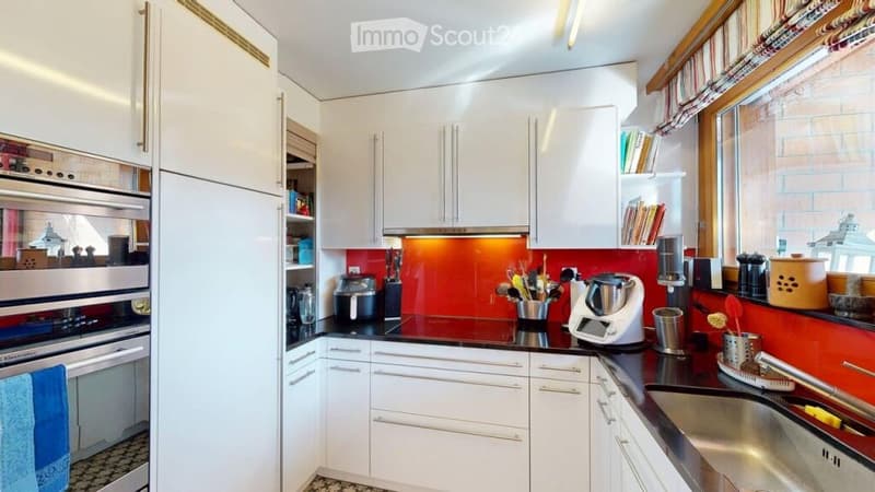 Modern kitchen with white cabinets, stainless steel appliances, and a red backsplash. Features include a refrigerator, oven, microwave, blender, toaster, sink, and various kitchen utensils.