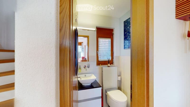 Modern bathroom with white walls, a white sink, a toilet, a mirror, and a wooden cabinet.
