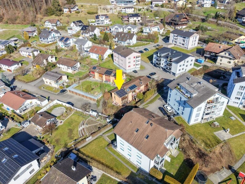 Aerial view of a residential neighborhood with multiple houses, solar panels on rooftops, and parked cars along the streets.