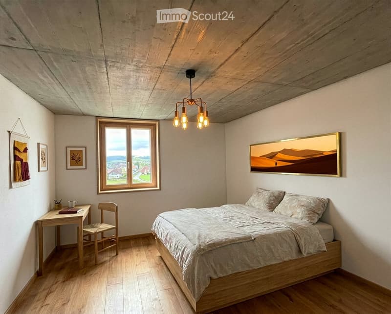 Cozy bedroom with wooden bed, desk, chair, and large window overlooking a scenic landscape.
