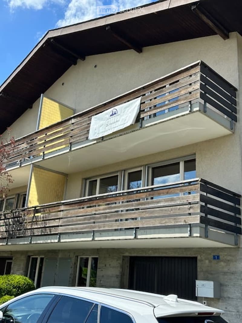 Two-story building with balconies, wooden railings, and a parked car in front.