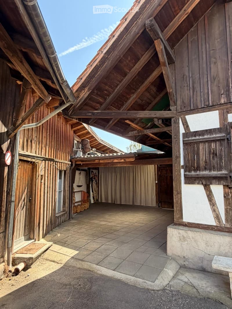 Courtyard with wooden beams, tiled floor, and wooden walls, featuring a covered area with a wooden roof and visible wooden beams.