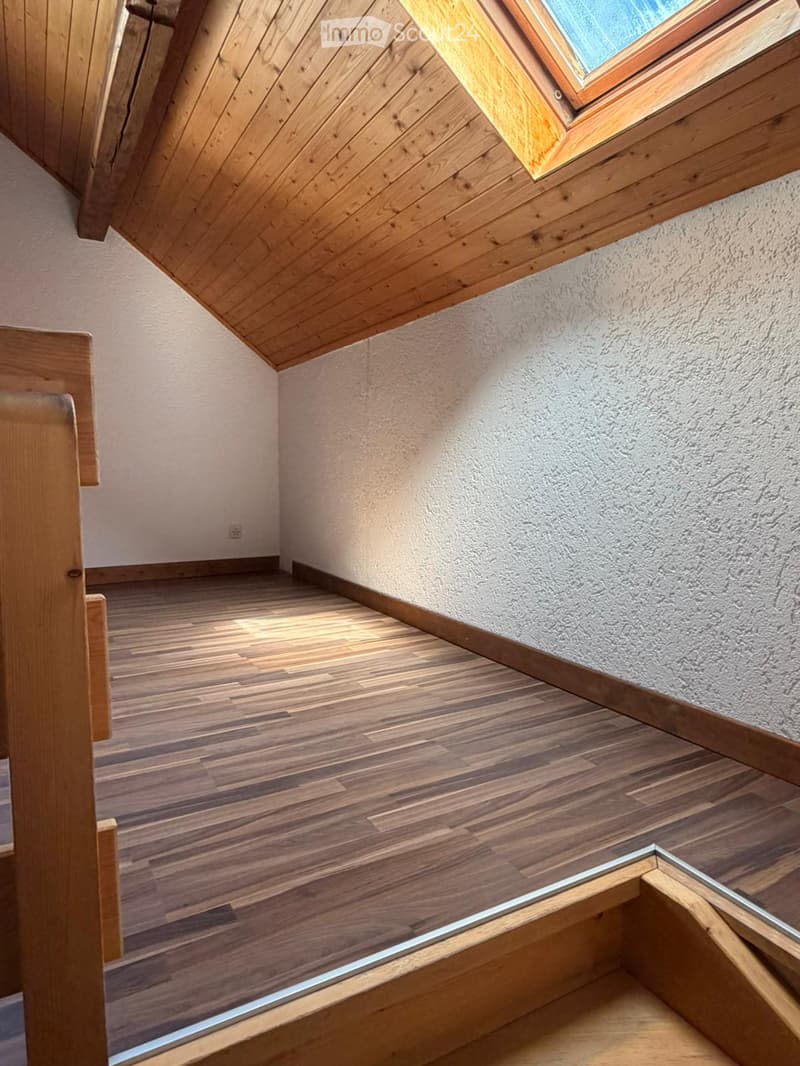 Empty attic space with wooden flooring, slanted wooden ceiling, and a skylight window. No furniture or equipment present.