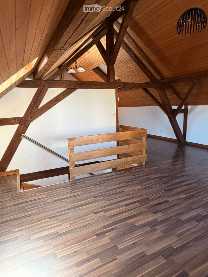 An empty attic space with exposed wooden beams, wooden flooring, and a small wooden bench against the wall.
