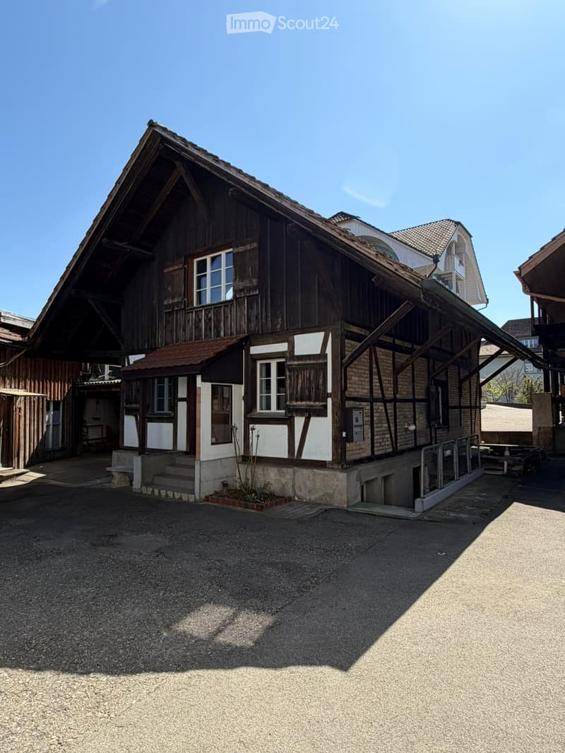 Traditional wooden building with a steep roof, white-painted sections, and a small porch with steps leading up to it.