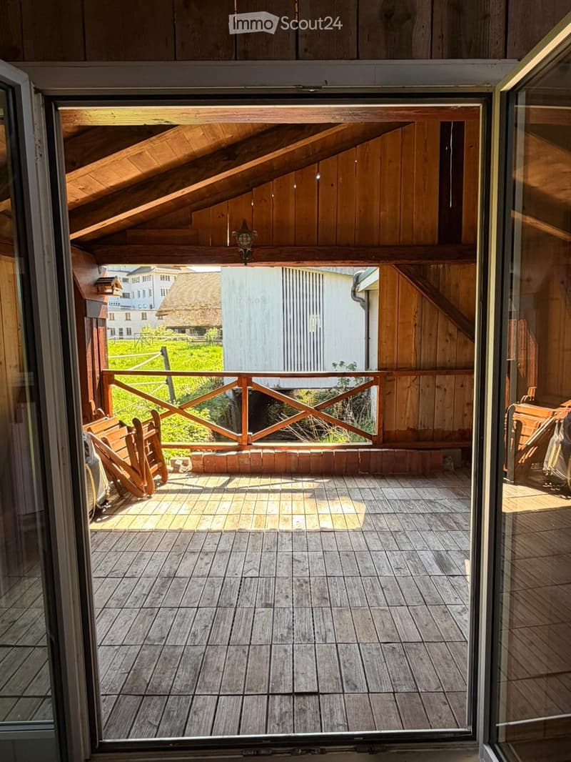 Wooden balcony with tiled floor, wooden railing, and a single wooden chair placed on the left side.