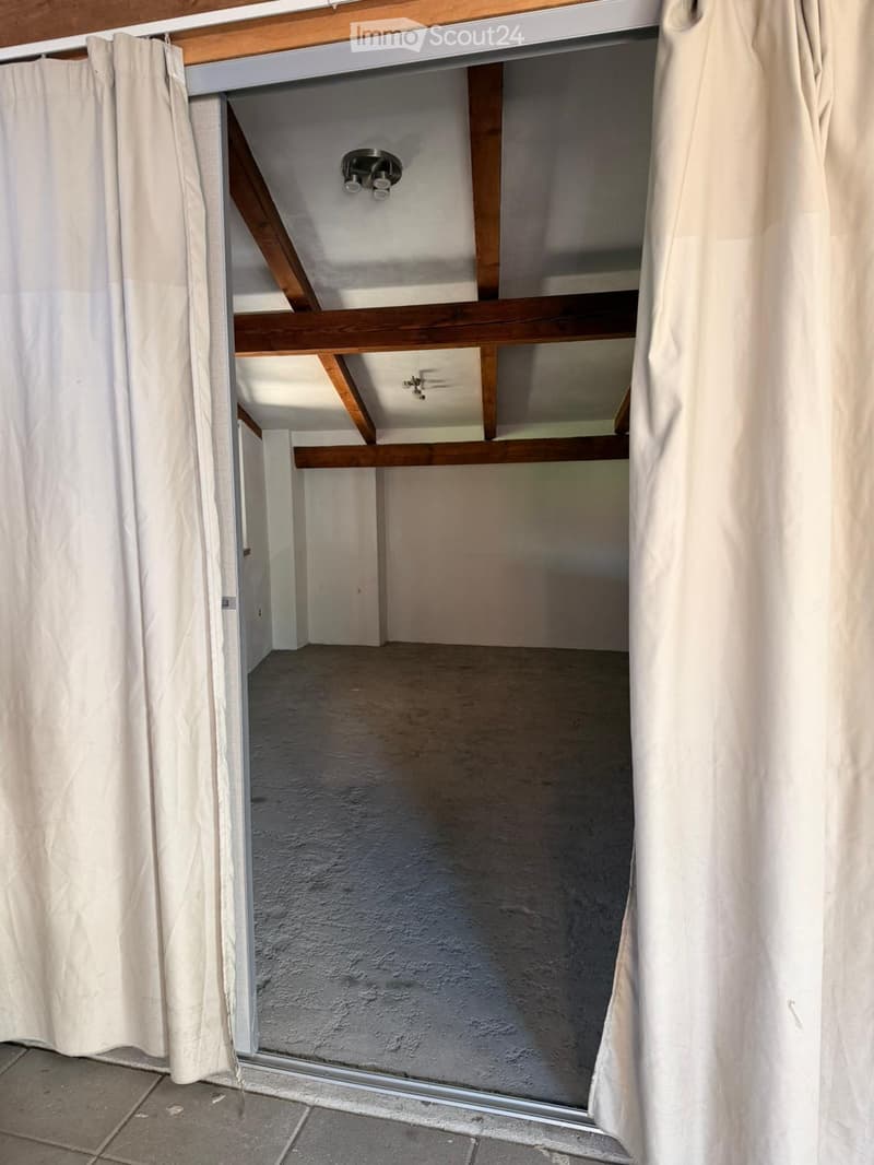 Empty room with wooden beams, exposed ceiling, and white curtains on either side of the doorway.
