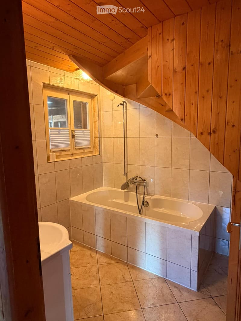 Bathroom with a bathtub, sink, and window, featuring wooden walls and a sloped ceiling.