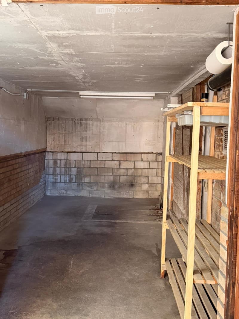 Empty storage room with concrete floor, brick walls, wooden shelving unit, and exposed pipes.