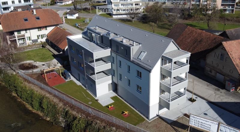 Modern multi-story residential building with grey exterior, multiple balconies, and a playground area in front.