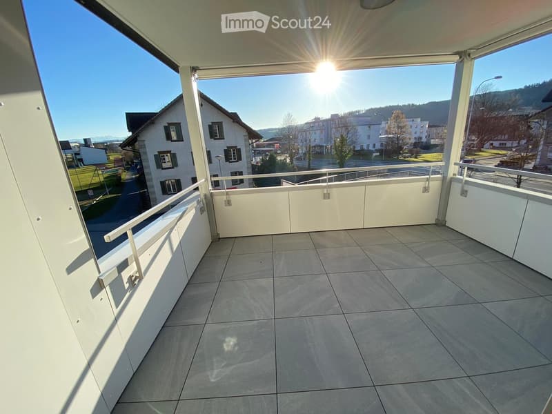 Balcony with tiled floor, white railings, and a view of a residential area with houses and greenery.