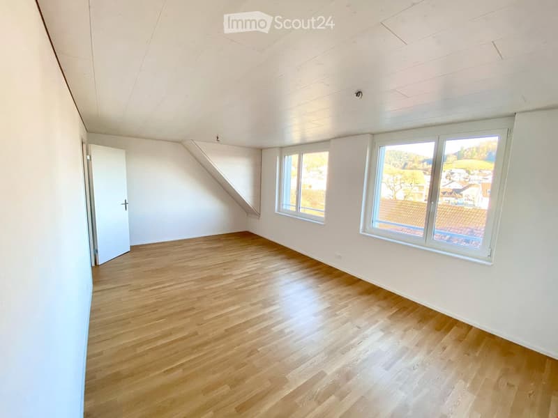 Empty room with wooden flooring, white walls, and large windows offering a scenic view of the surrounding area.