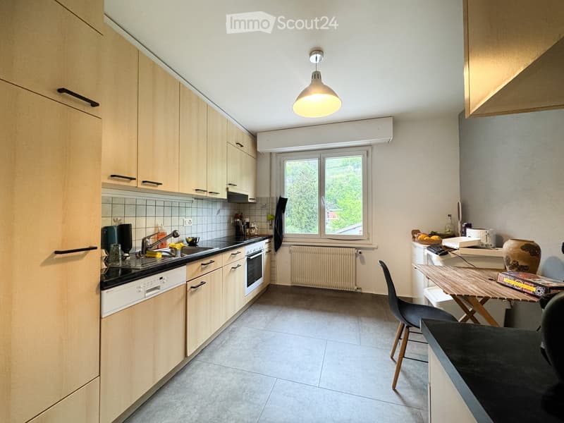 Modern kitchen with light wood cabinets, stainless steel appliances, and a central island with a dining area.