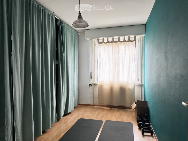 A room with wooden flooring, green curtains, and exercise mats on the floor, with dumbbells placed against the wall.