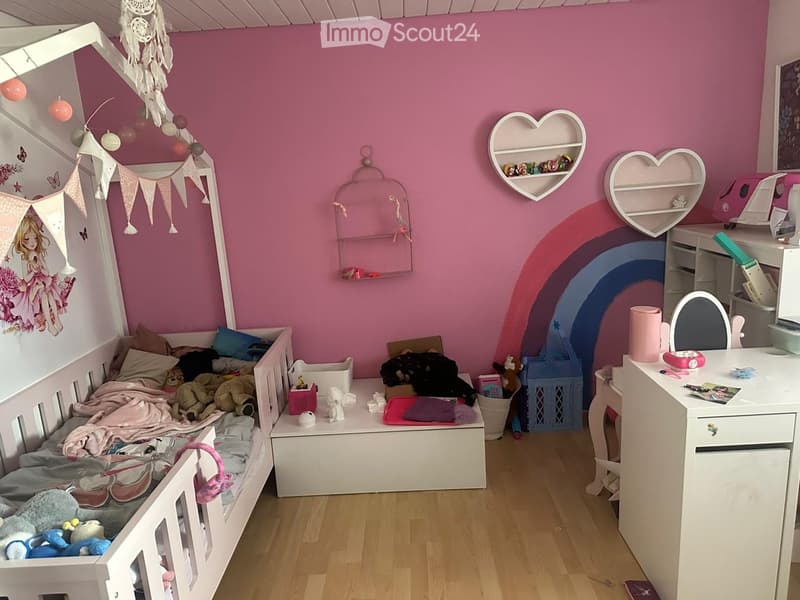 A colorful children's bedroom with a white wooden bed, a desk with a mirror, shelves, and various toys and decorations.