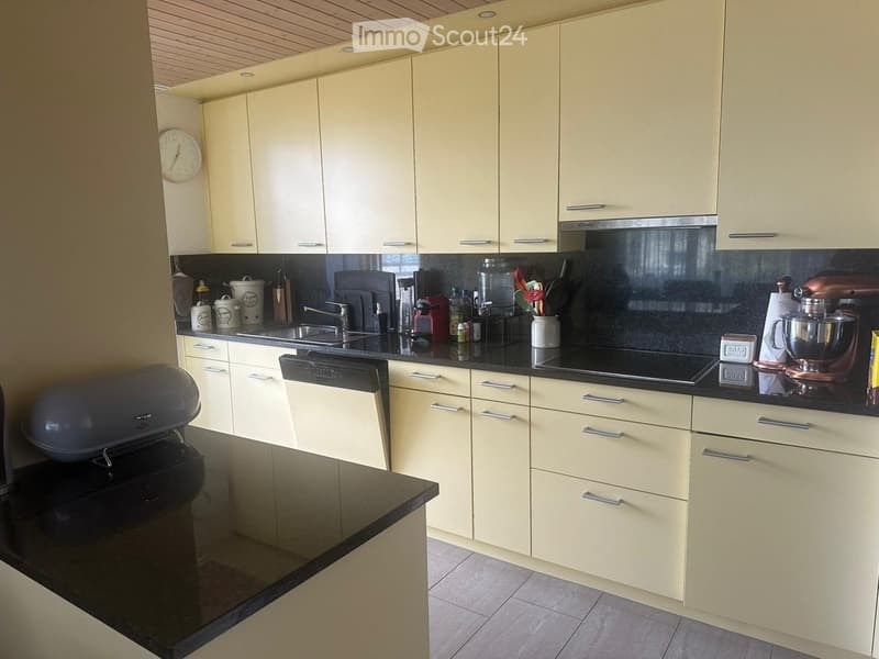 Modern kitchen with light-colored cabinets, black countertops, and various appliances including a sink, oven, dishwasher, and mixer.