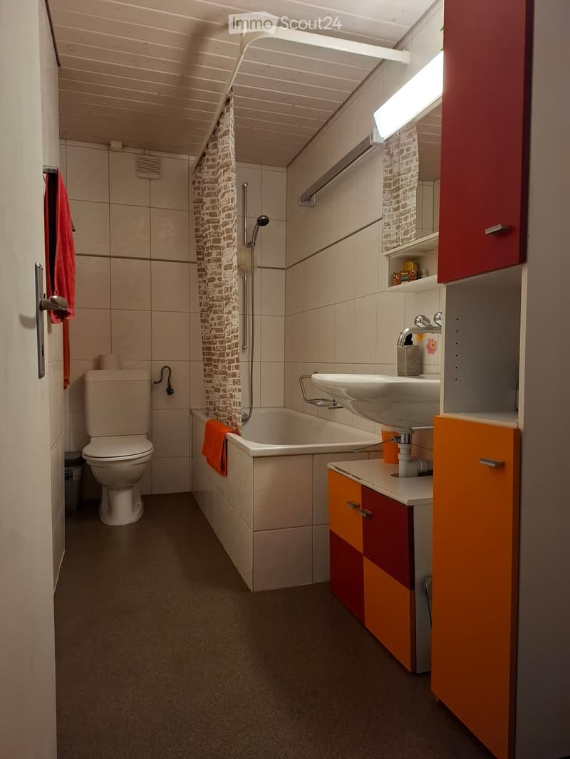 Bathroom with a toilet, bathtub, sink, mirror, and colorful cabinets. Features a shower curtain and towels.