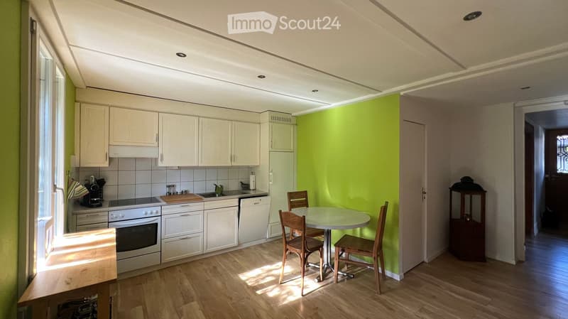 Bright kitchen with white cabinets, wooden floor, and a small dining area with a round table and chairs. Appliances include an oven, dishwasher, and coffee maker.