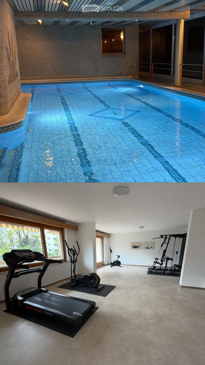 Indoor swimming pool with blue tiles and a modern ceiling design, surrounded by wooden decking and glass walls.