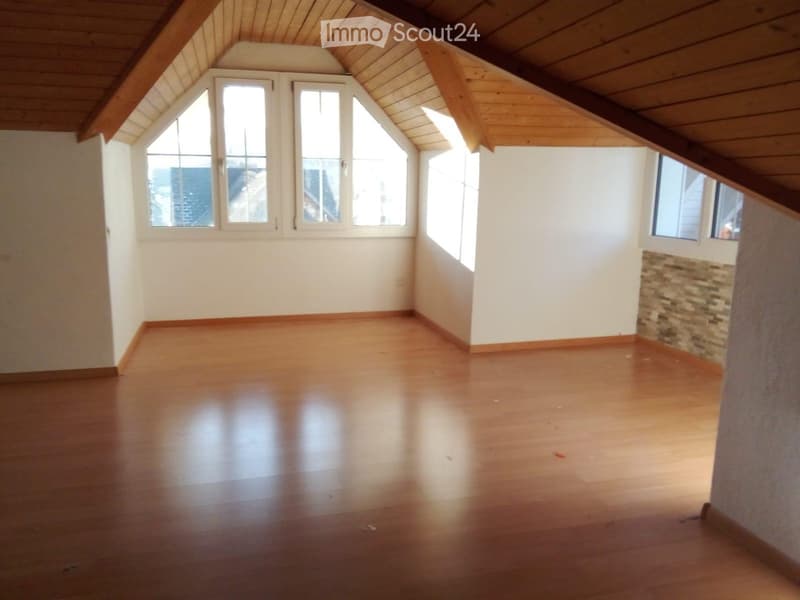 Empty attic room with wooden floors, white walls, and multiple windows allowing natural light. The ceiling has exposed wooden beams and a sloped design.