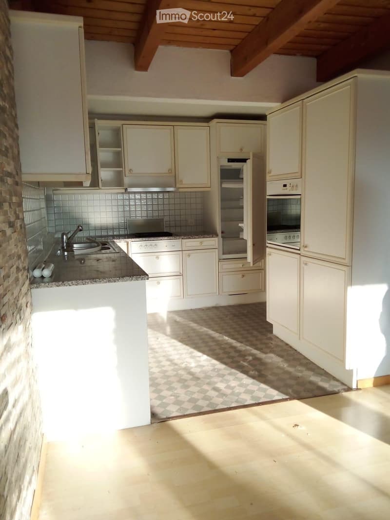 Bright kitchen with white cabinets, stainless steel appliances, and a stone-tiled backsplash. Features a central island with a sink and faucet, and a built-in oven with a microwave above it.