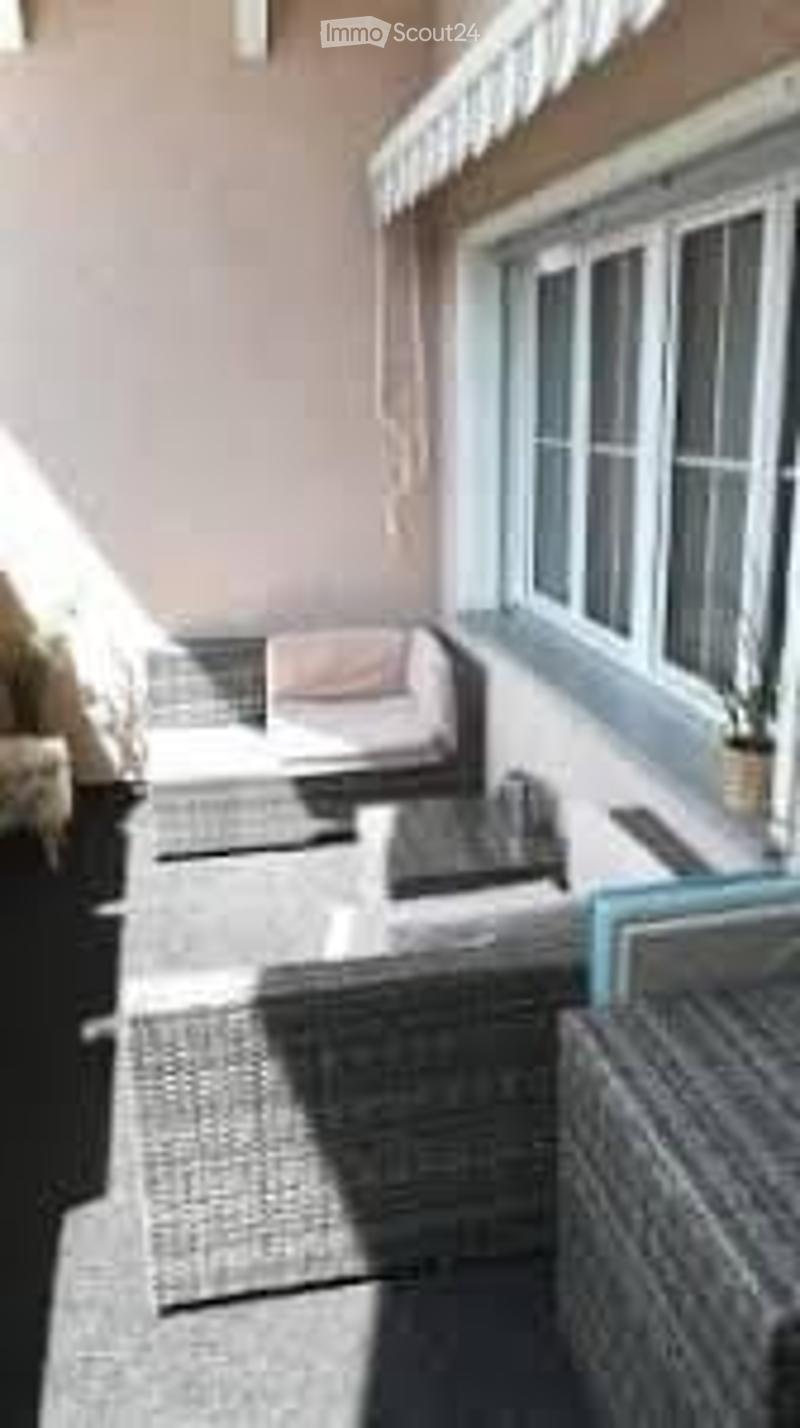 Balcony with outdoor furniture including a sofa, chairs, and a coffee table, with large windows and a view of the surrounding area.