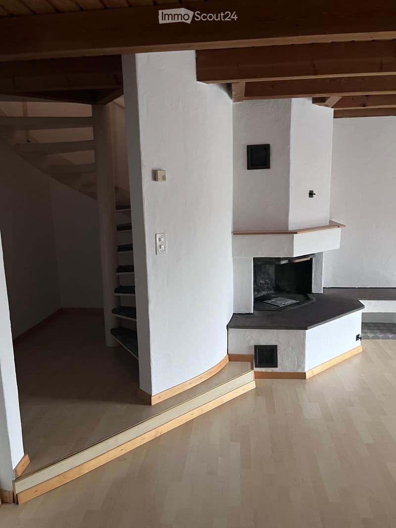 Empty hallway with wooden flooring, white walls, and a built-in fireplace with a black hearth and white surround.