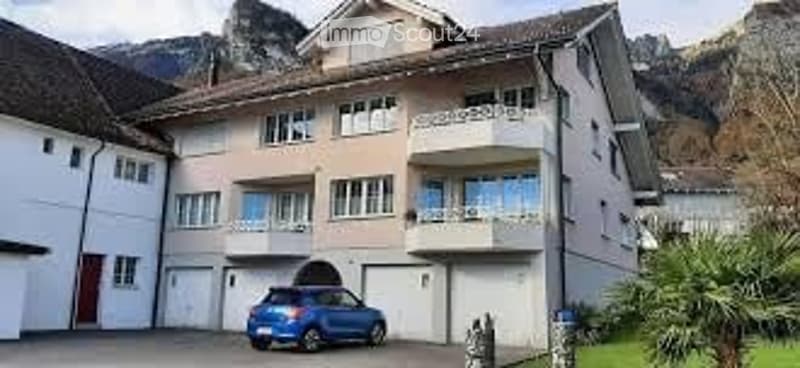 Multi-story residential building with balconies, garage, and a blue car parked in front.