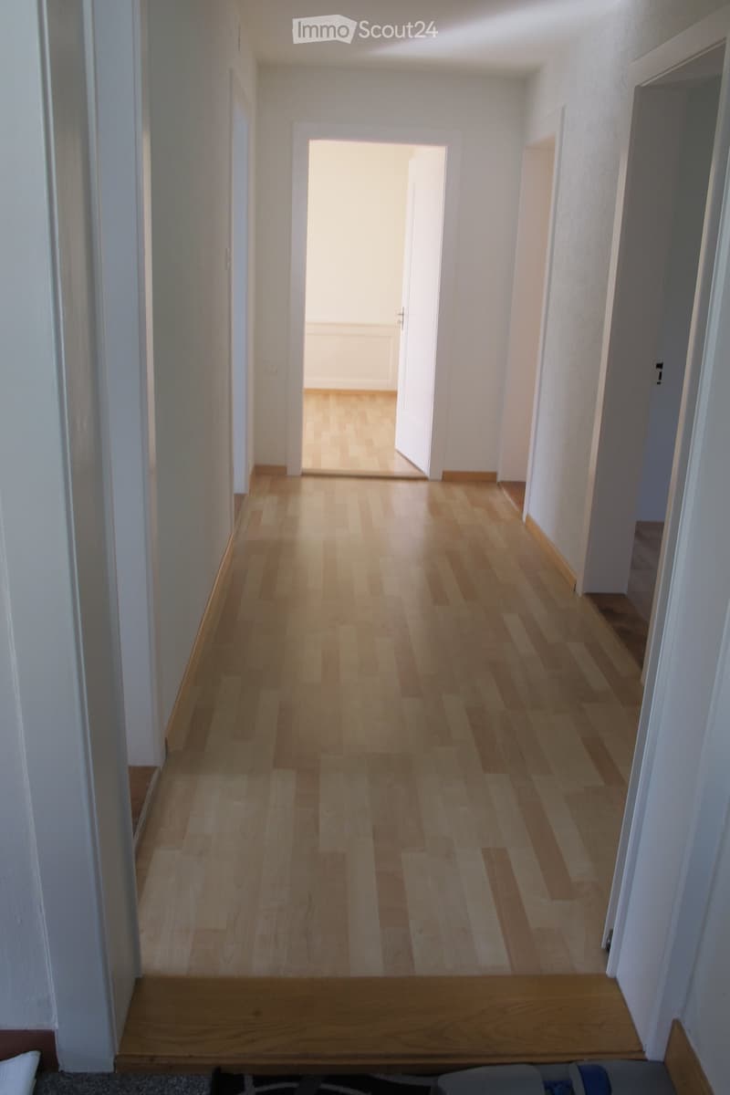 Empty hallway with wooden floor, white walls, and open doors leading to rooms.