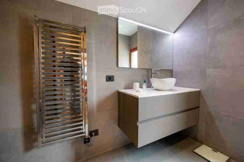 Modern bathroom with a sleek sink, mirror, and cabinet. The walls are tiled in neutral tones, and the floor is tiled as well.