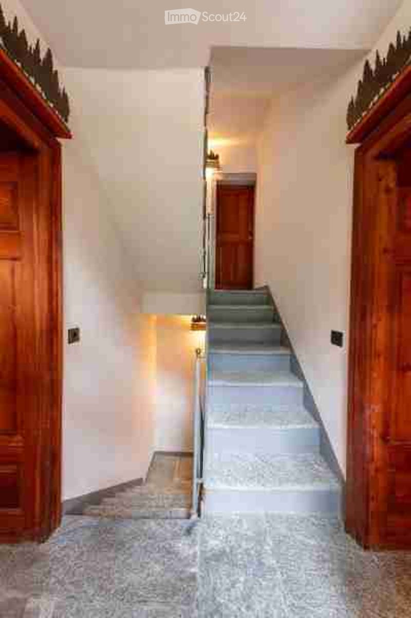 Spacious hallway with a staircase leading upwards, wooden paneling on both sides, and neutral-colored walls.