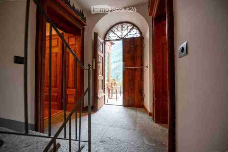 A narrow hallway with arched doorways, wooden doors, and a metal railing leading to an outdoor area.