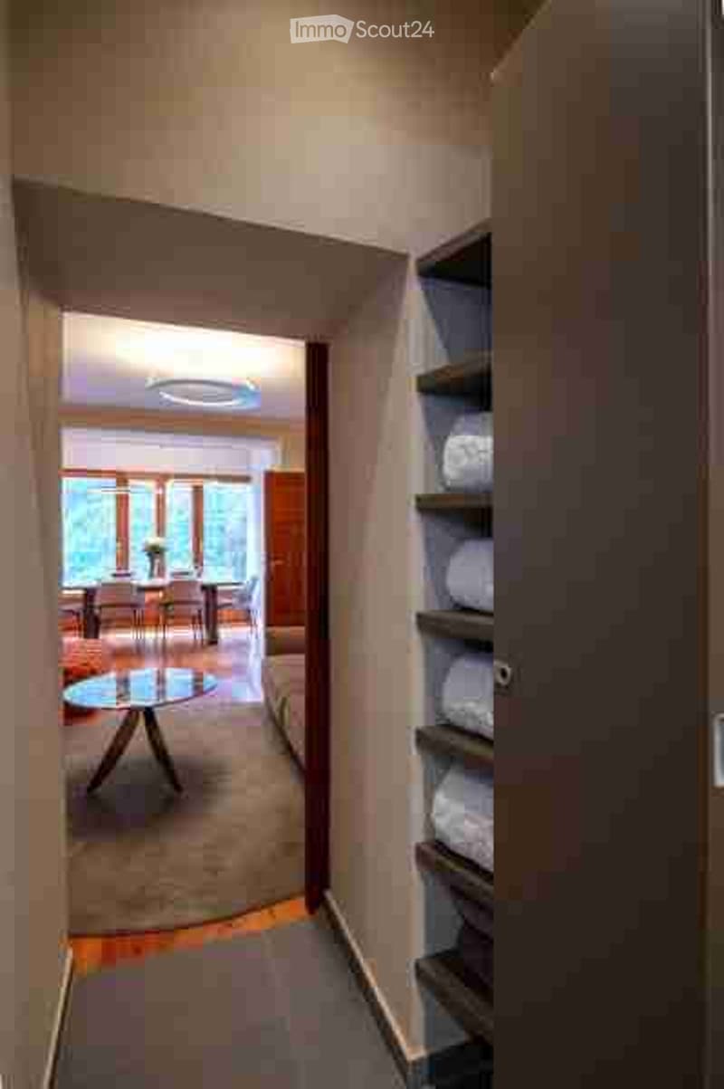 A modern hallway with a round glass coffee table, leading to a dining area with chairs and a table, and a living area with a sofa.
